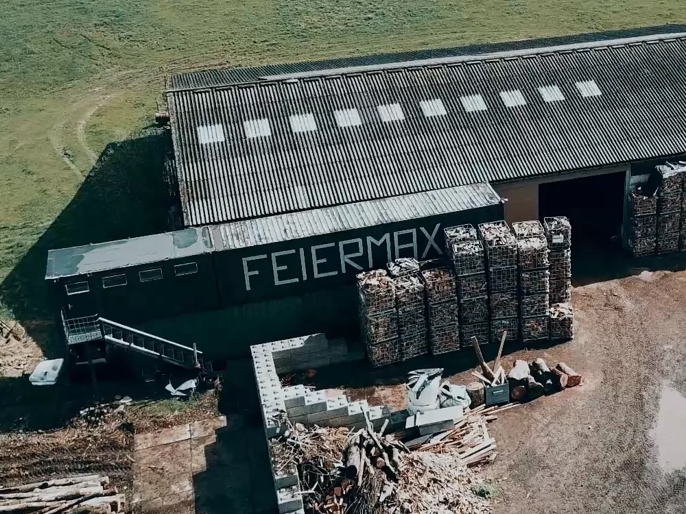 Luftaufnahme des FEIERMAX-Lagers: FEIERMAX-Schriftzug an der Fassade, mit Brennholz gefüllte Gitterboxen
